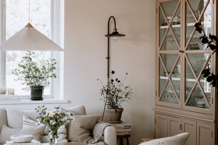 Nástenná lampa Cobbler s tienidlom z dymového plisovaného skla v obývačke vedľa vysokej presklenej vitríny.