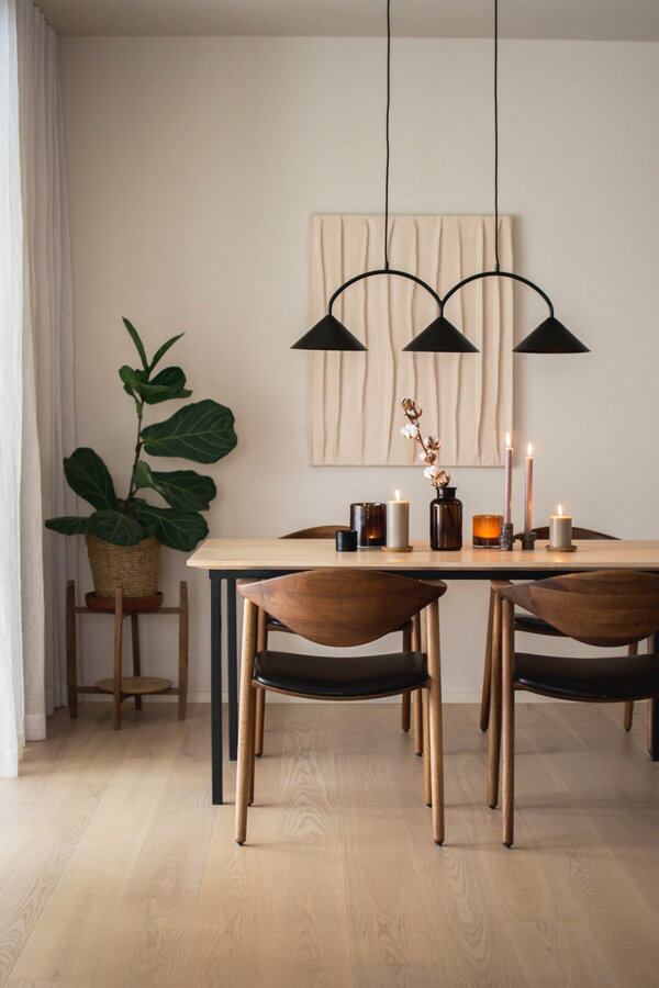 Čierna závesná lampa s troma trojuholníkovými tienidlami nad prestretým jedálenským stolom.