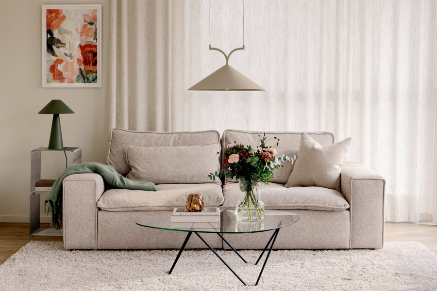 Béžová závesná lampa s trojuholníkovým tienidlom nad konferenčným stolíkom v obývačke s béžovou pohovkou.