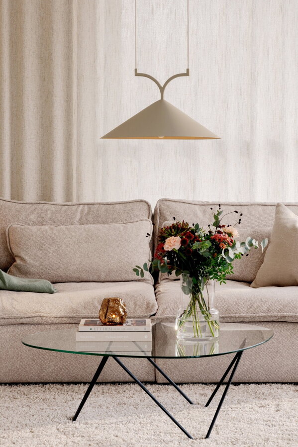 Béžová závesná lampa s trojuholníkovým tienidlom nad konferenčným stolíkom v obývačke s béžovou pohovkou.