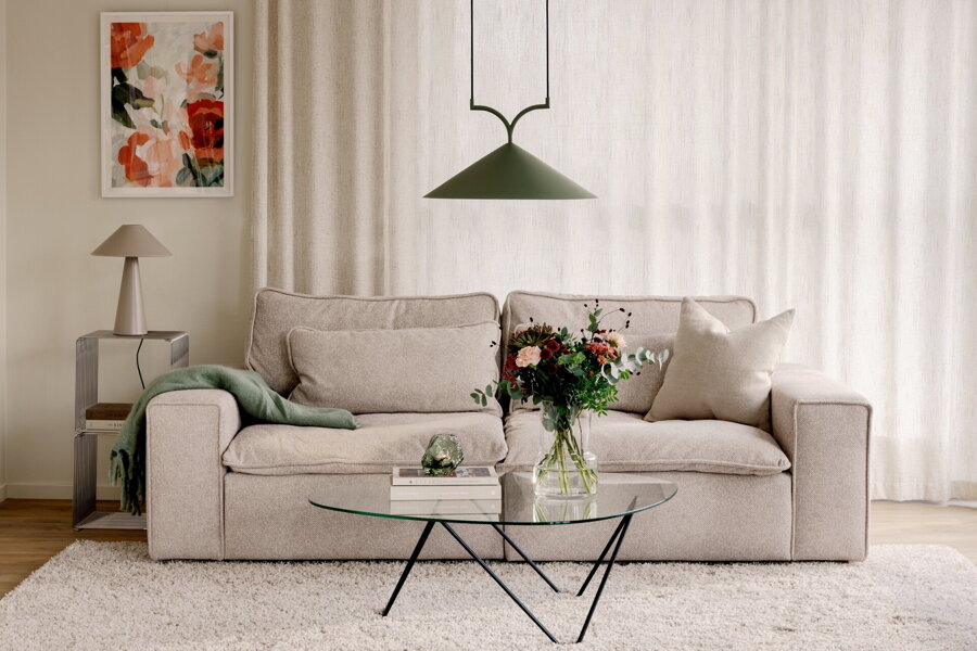 Zelená závesná lampa s trojuholníkovým tienidlom nad konferenčným stolíkom v obývačke s béžovou pohovkou.