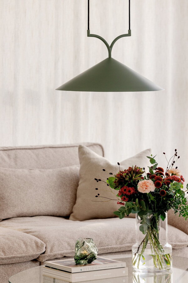 Zelená závesná lampa s trojuholníkovým tienidlom nad preskleným konferenčným stolíkom, na ktorom je váza s kyticou kvetou.