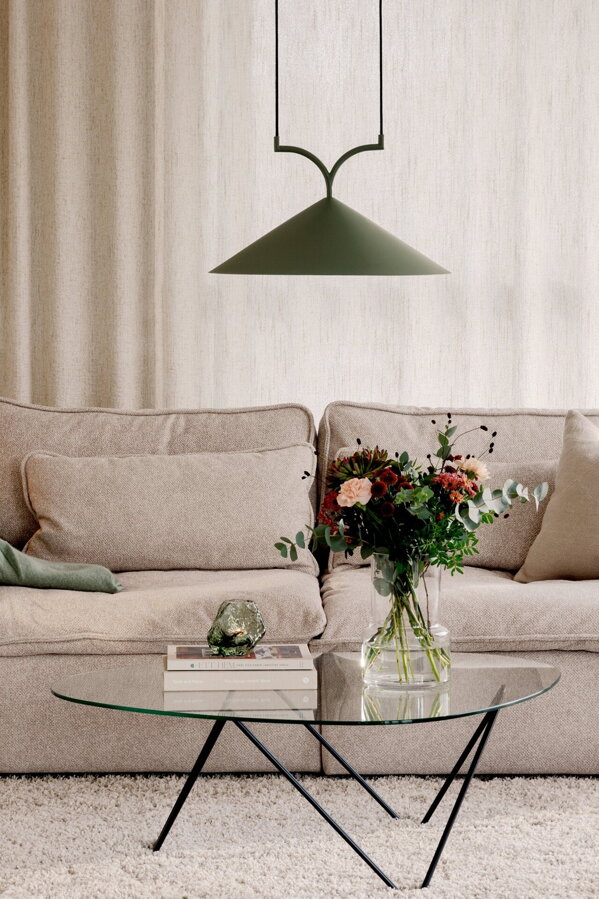 Zelená závesná lampa s trojuholníkovým tienidlom nad preskleným konferenčným stolíkom, na ktorom je váza s kyticou kvetou.