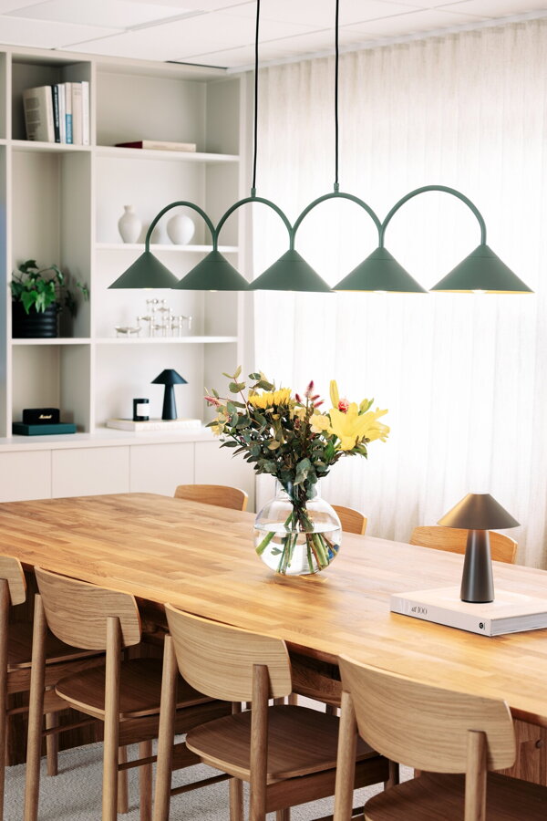 Svietiaca zelená závesná lampa s piatimi trojuholníkovými tienidlami nad prestretým jedálenským stolom.
