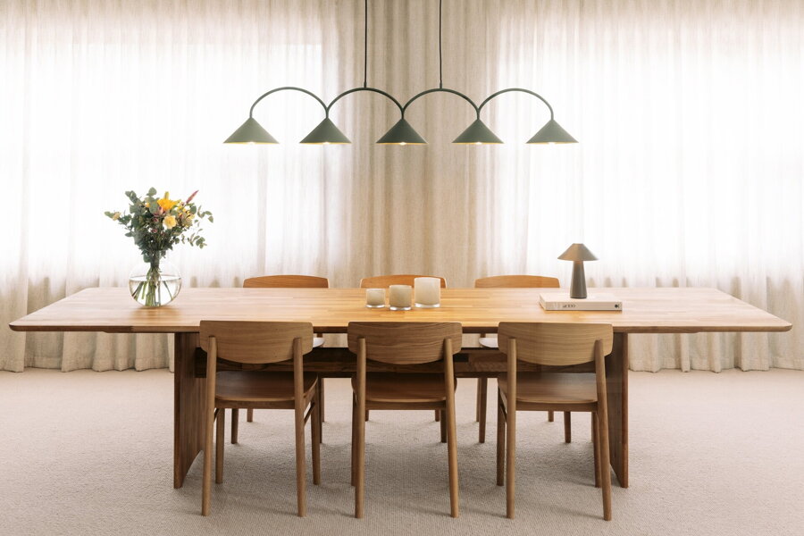 Svietiaca zelená závesná lampa s piatimi trojuholníkovými tienidlami nad prestretým jedálenským stolom.