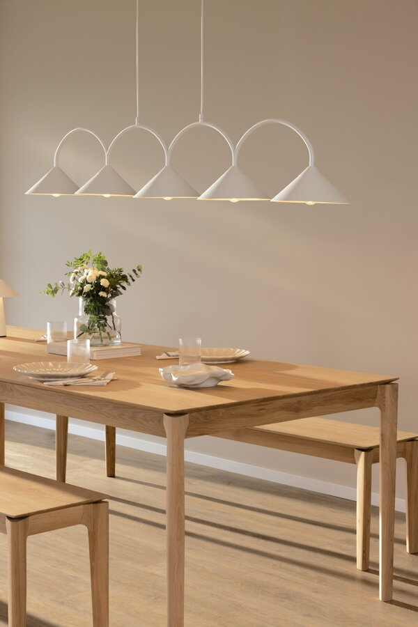 Svietiaca biela závesná lampa s piatimi trojuholníkovými tienidlami nad jedálenským stolom.