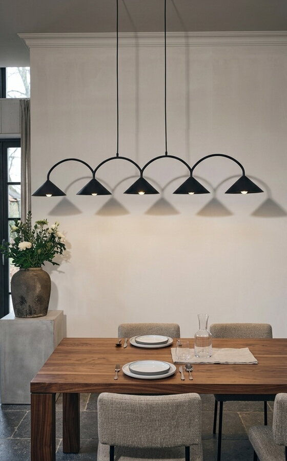 Svietiaca čierna závesná lampa s piatimi trojuholníkovými tienidlami nad prestretým jedálenským stolom.