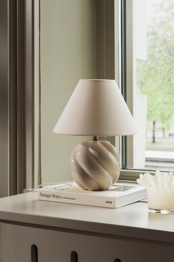 Béžová stolová lampa s vlnitou keramickou základňou na parapete okna.