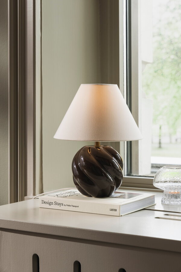 Hnedá stolová lampa s vlnitou keramickou základňou na parapete okna.