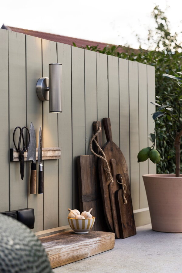 Hliníková nástenná lampa s obojsmerným svietením vo farbe brúsenej ocele, zavesená na drevenej stene na terase.