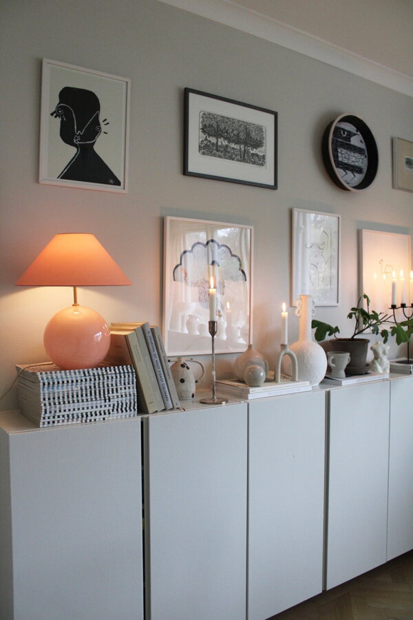 Svetloružová stolová lampa na bielej komode s knihami a dekoráciami.