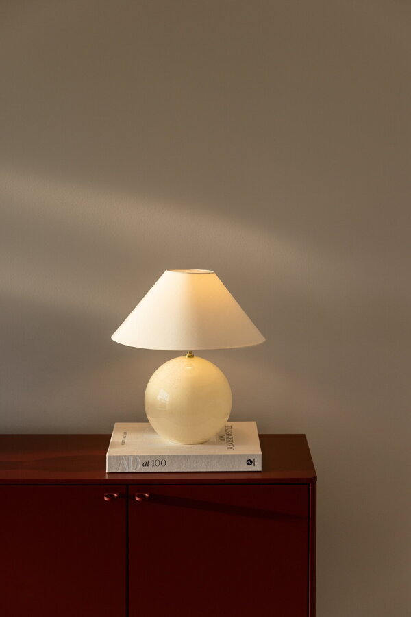 Svietiaca stolová lampa Iris s guľovitou základňou z ručne fúkaného skla a bavlneným tienidlom v krémovej farbe.