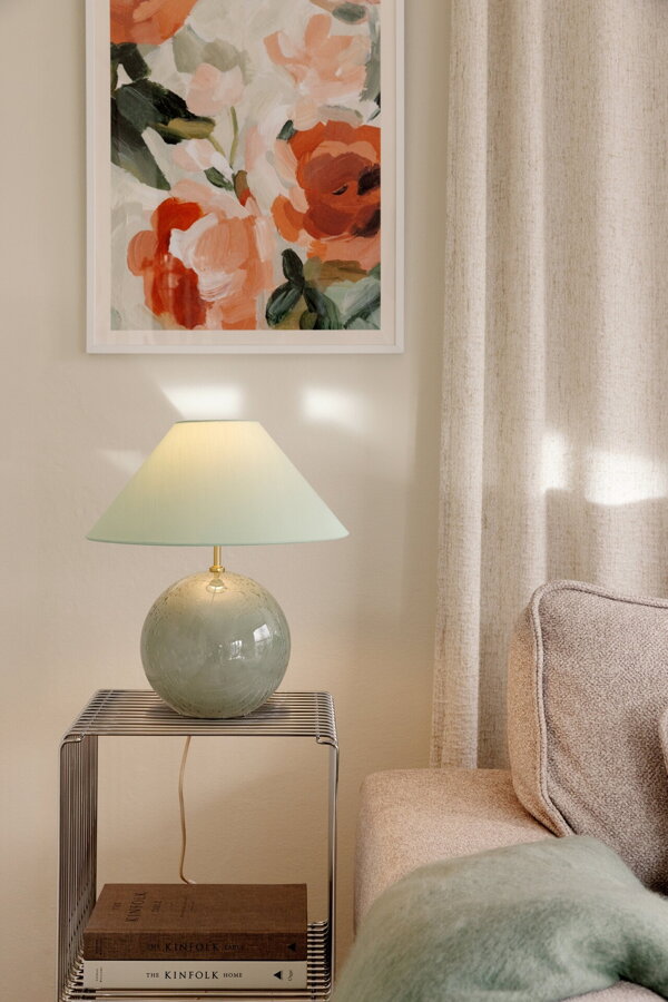 Zelená stolová lampa na príručnom stolíku v obývačke vedľa béžovej pohovky.