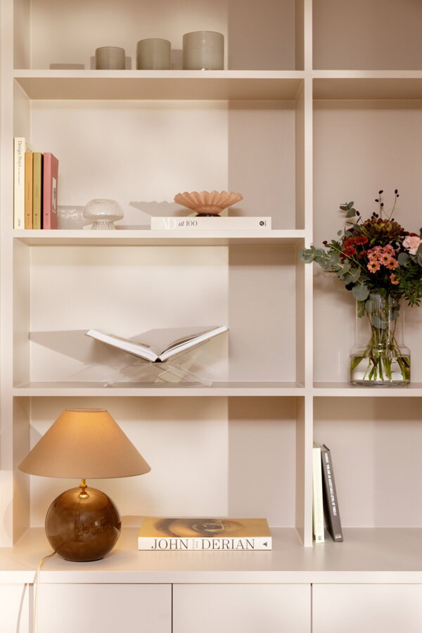 Hnedá stolová lampa Iris na spodnej polici bieleho policového regálu.