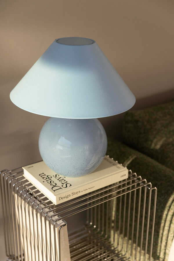 Svetlomodrá stolová lampa položená na knihe na kovovom príručnom stolíku.