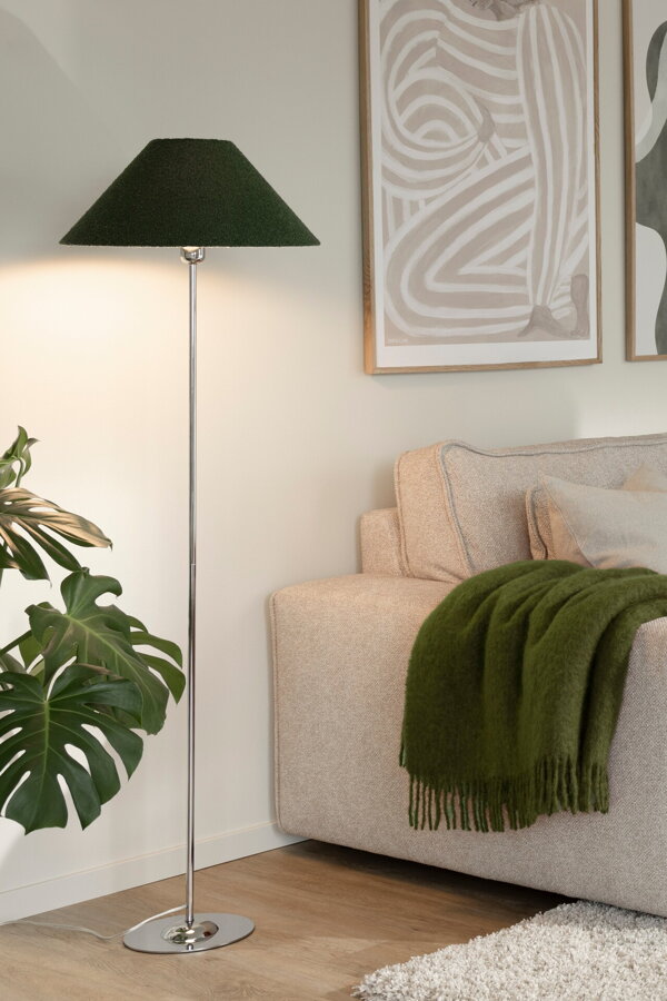 Svietiaca kovová stojanová lampa so zeleným textilným tienidlom vedľa béžovej pohovky.