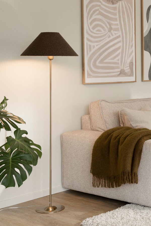 Svietiaca kovová stojanová lampa s hnedým textilným tienidlom vedľa béžovej pohovky.