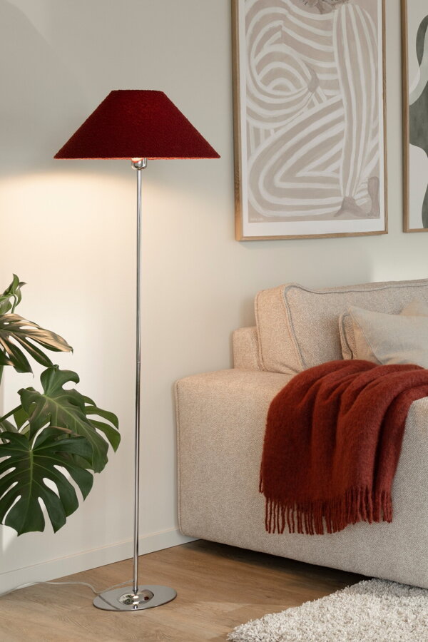 Svietiaca kovová stojanová lampa s tmavočerveným textilným tienidlom vedľa béžovej pohovky.