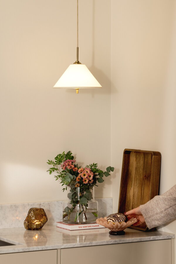 Svietiaca závesná lampa Iris krémovej farby nad kuchynskou linkou.