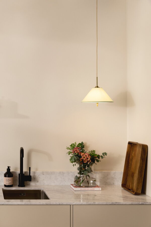 Svietiaca závesná lampa Iris s bavlneným tienidlom jemnej zelenej farby nad kuchynskou linkou.