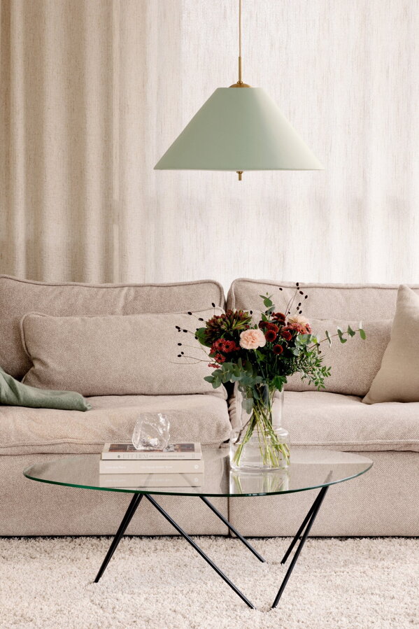 Svietiaca závesná lampa Iris s bavlneným tienidlom jemnej zelenej farby v obývačke nad preskleným konferenčným stolíkom s vázou s kyticou kvetou.