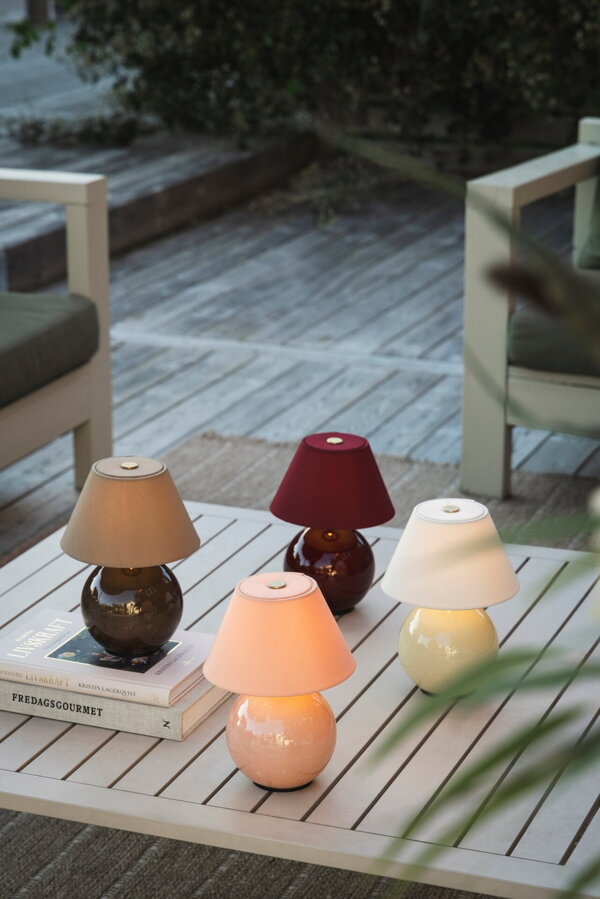 Štyri prenosné stolové lampy v hnedej, ružovej, tmavočervenej a krémovej farbe, na stolíku na terase.