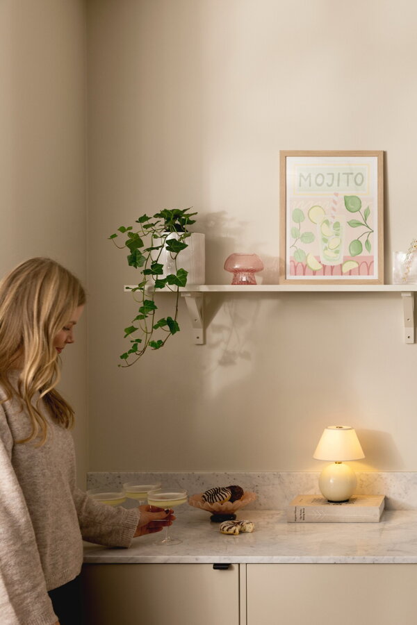 Béžová svietiaca prenosná stolová lampa Iris položená na knihe na kuchynskej linke.