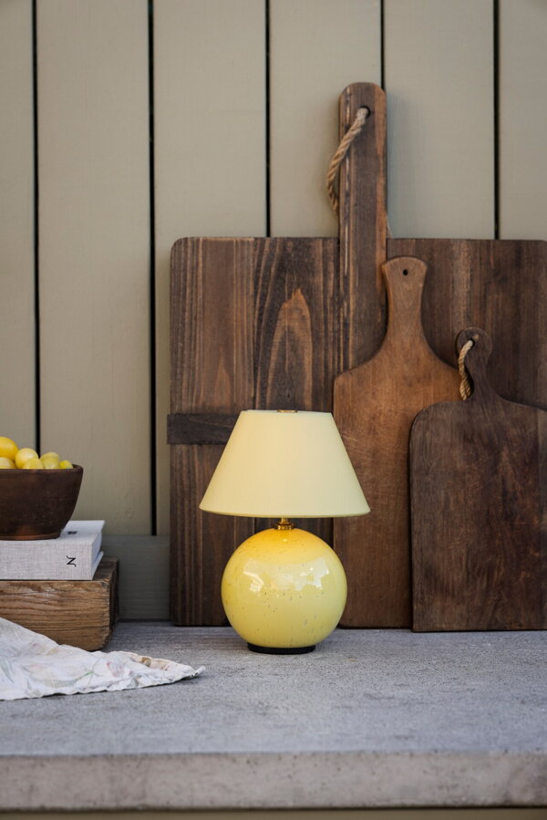 Svetložltá prenosná stolová lampa Iris položená na záhradnej kuchynskej linke vedľa krájacej dosky.