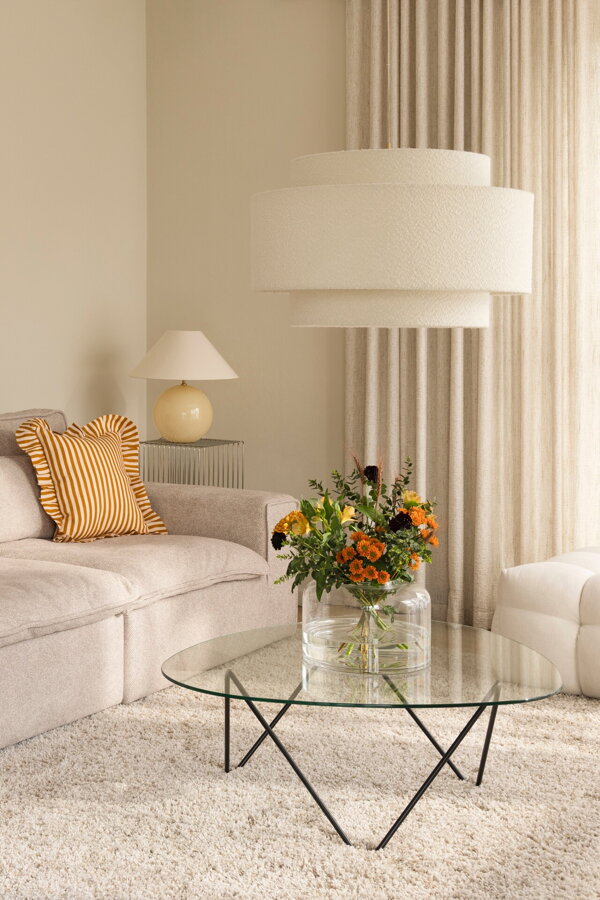 Závesná lampa Noah s bielym tienidlom z tkaniny bouclé a prvkami v prevedení pravej mosadze v obývačke s béžovou sedačkou.