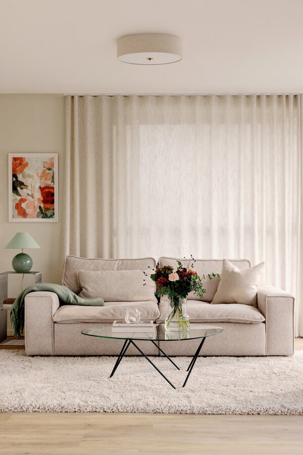 Stropná lampa Noah s béžovým tienidlom z kvalitného ľanu a prvkami v prevedení pravej mosadze v obývačke nad béžovou sedačkou.