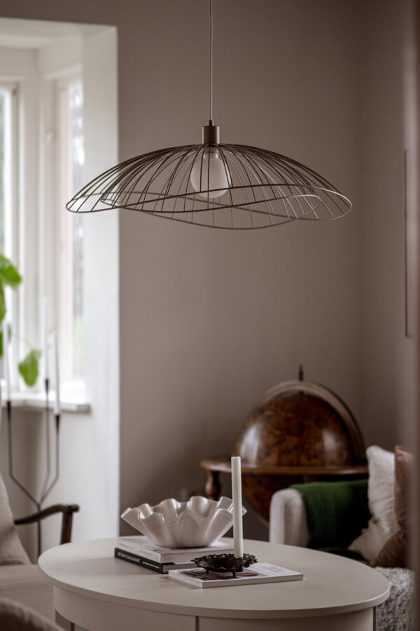 Dizajnová závesná lampa Ray s kovovým tienidlom v hnedosivej farbe v obývačke nad stolom s bielym obrusom.