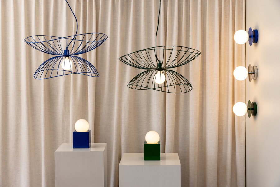 Viacero modrých svietidiel rôzneho druhu od závesných, stolových a nástenných, ktoré su rozložené na bielych podstavcoch.