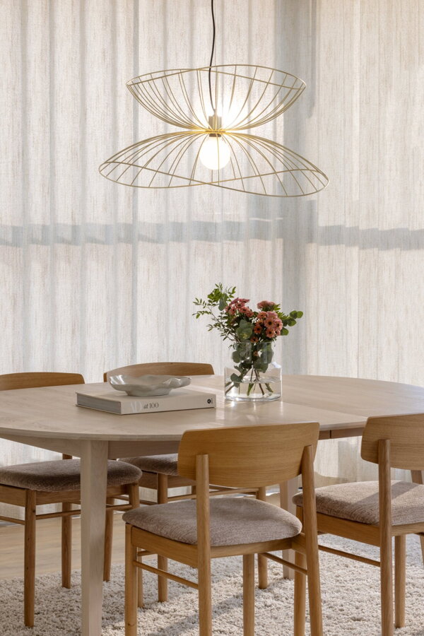 Kovová závesná lampa vo farbe brúsenej mosadze nad jedálenským stolom.