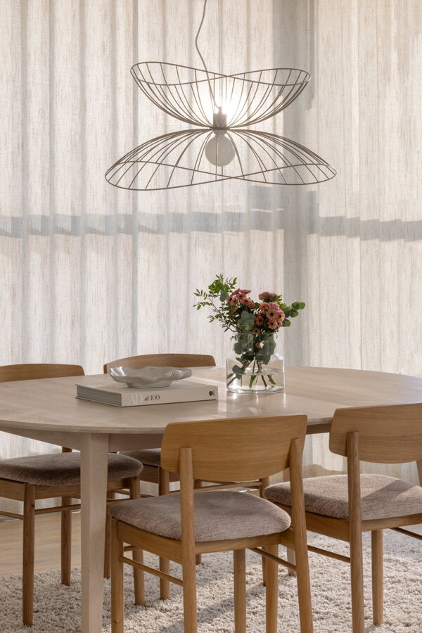 Kovová závesná lampa vo farbe brúsenej mosadze nad jedálenským stolom.