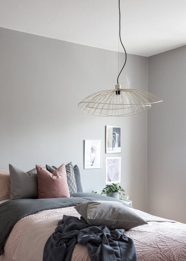 Kovová závesná lampa vo farbe brúsenej mosadze v spálni nad posteľou.