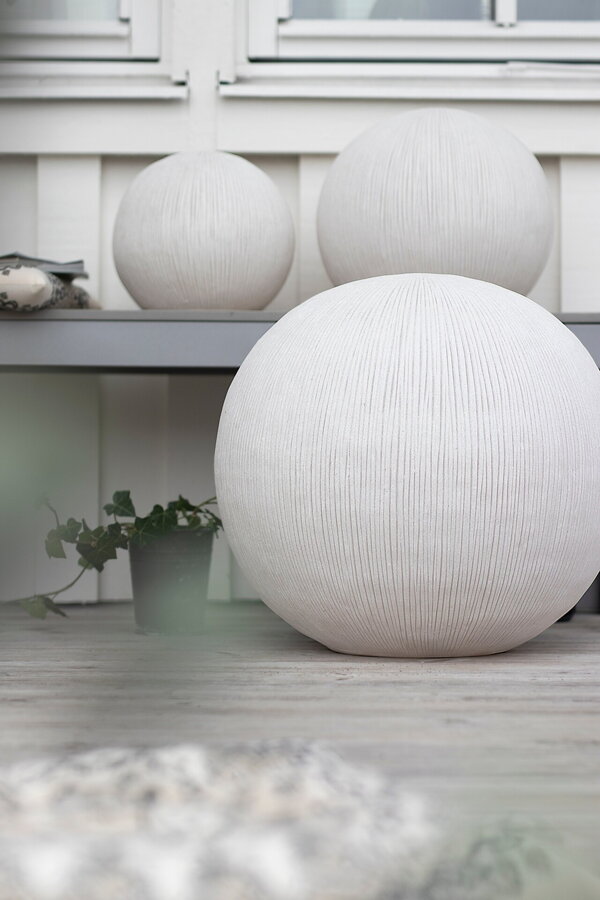 Tri biele okrúhle exteriérové lampy rôznych veľkostí na terase bielej farby.