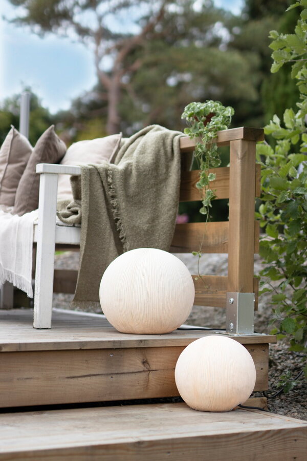 Dve svietiace biele guľaté vonkajšie lampy v záhrade vedľa záhradnej pohovky.