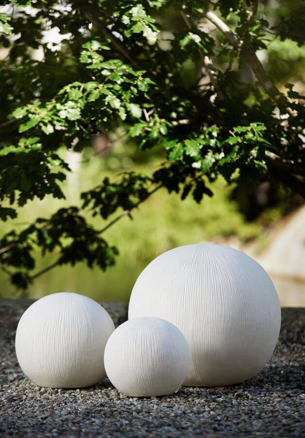 Tri biele okrúhle exteriérové lampy na asfaltovom povrchu pod korunou stromu.