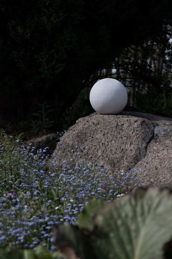Biela exteriérová lampa v tvare gule na veľkom kameni.