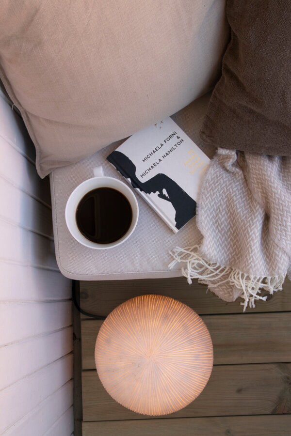 Biela exteriérová lampa v tvare gule na podlahe vedľa príručného stolíka so šálkou kávy.