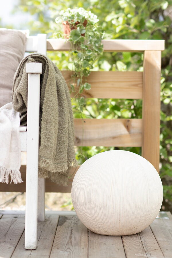 Biela okrúhla vonkajšia lampa na terase vedľa záhradného kresla.