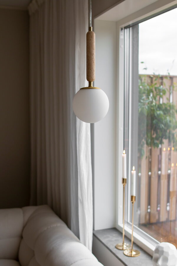 Závesná lampa Torrano s masívnou travertínovou základňou a s jemným tienidlom z bieleho opálového skla visiaca zo stropu vedľa okna.