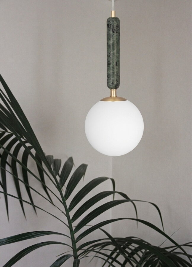 Luxusná závesná lampa Torrano s tmavozelenou mramorovou základňou a s jemným tienidlom z bieleho opálového skla nad izbovou rastlinou.