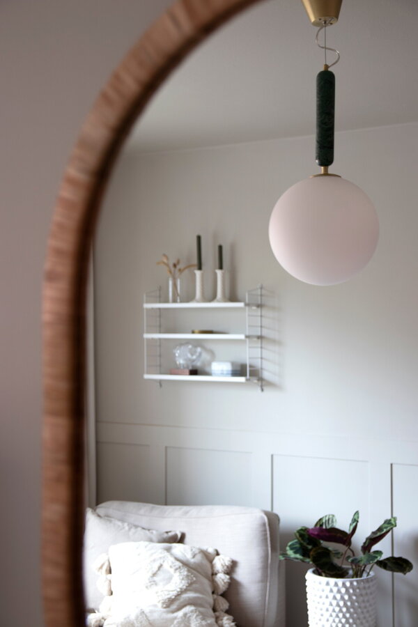 Závesná lampa Torrano s tmavozelenou mramorovou základňou a s jemným tienidlom z bieleho opálového skla v obývačke.