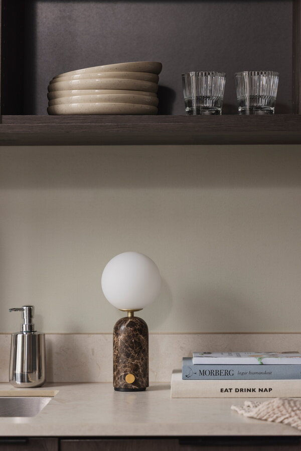 Prenosná stolová lampa Torrano s masívnou hnedou mramorovou základňou a s jemným tienidlom z bieleho opálového skla na kuchynskej linke.