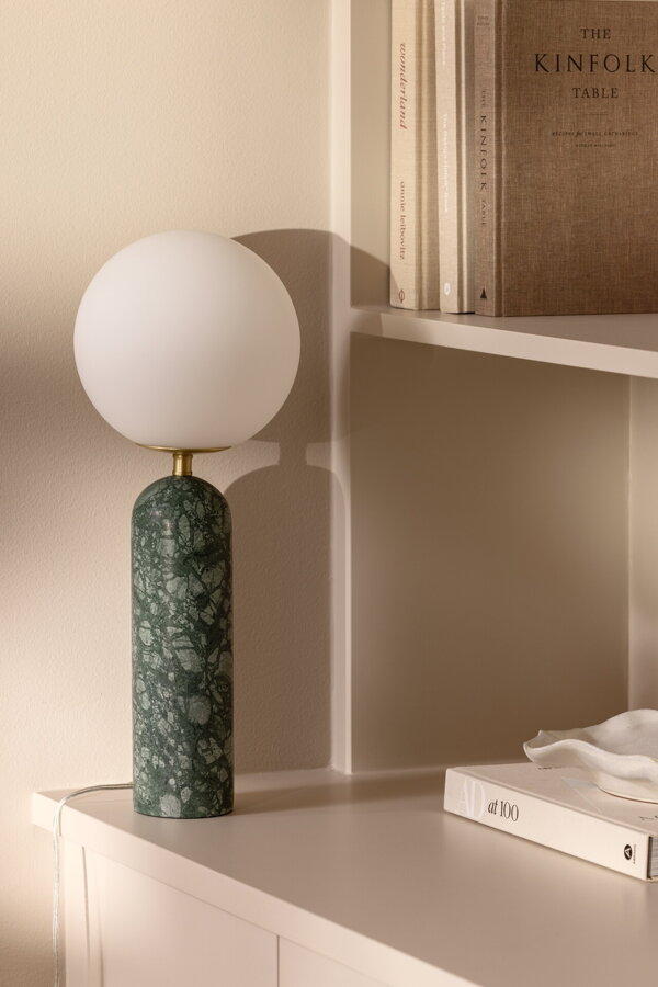 Stolová lampa Torrano s tmavozelenou mramorovou základňou a s jemným tienidlom z bieleho opálového skla, na bielej skrinke.
