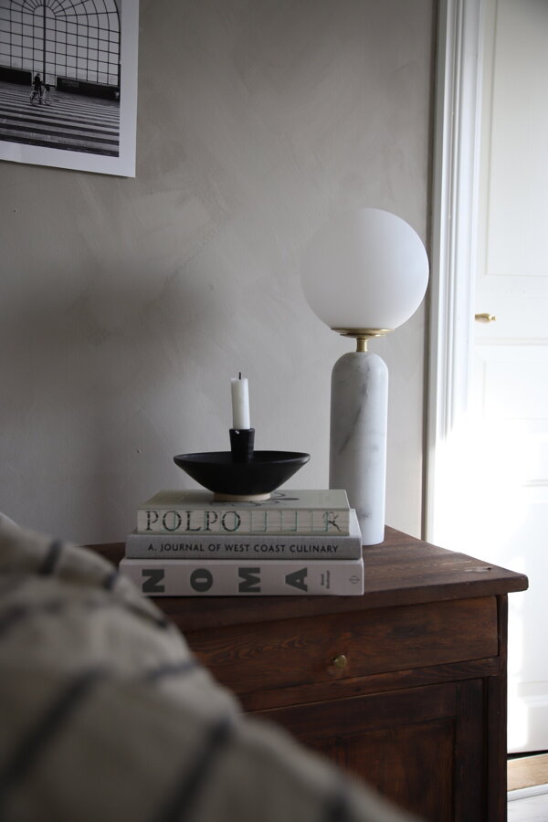 Biela mramorová stolová lampa Torrano s jemným tienidlom z bieleho opálového skla na hnedej drevenej skrinke.