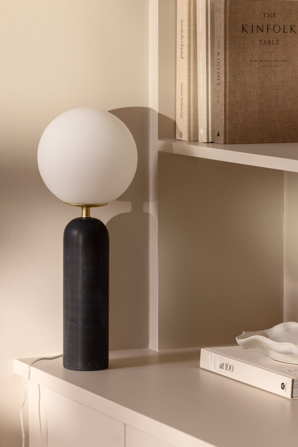 Stolová lampa Torrano s čiernou mramorovou základňou a s jemným tienidlom z bieleho opálového skla, na bielej skrinke.