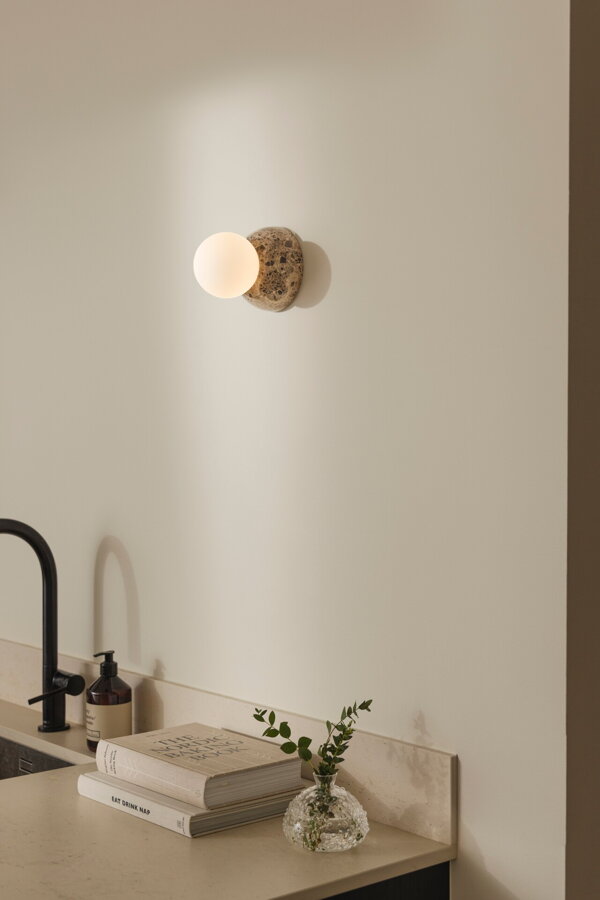 Nástenná lampa Torrano s masívnou hnedou mramorovou základňou a s jemným tienidlom z bieleho opálového skla v kuchyni nad umývadlom..