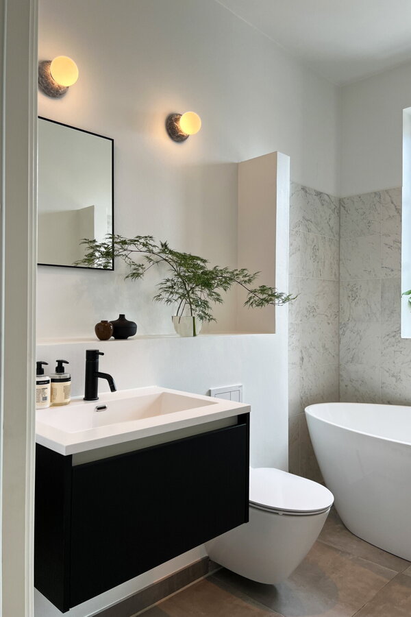 Dve svietiace nástenné sivé mramorové lampy s opálovým tienidlom nad umývadlom v kúpeľni.